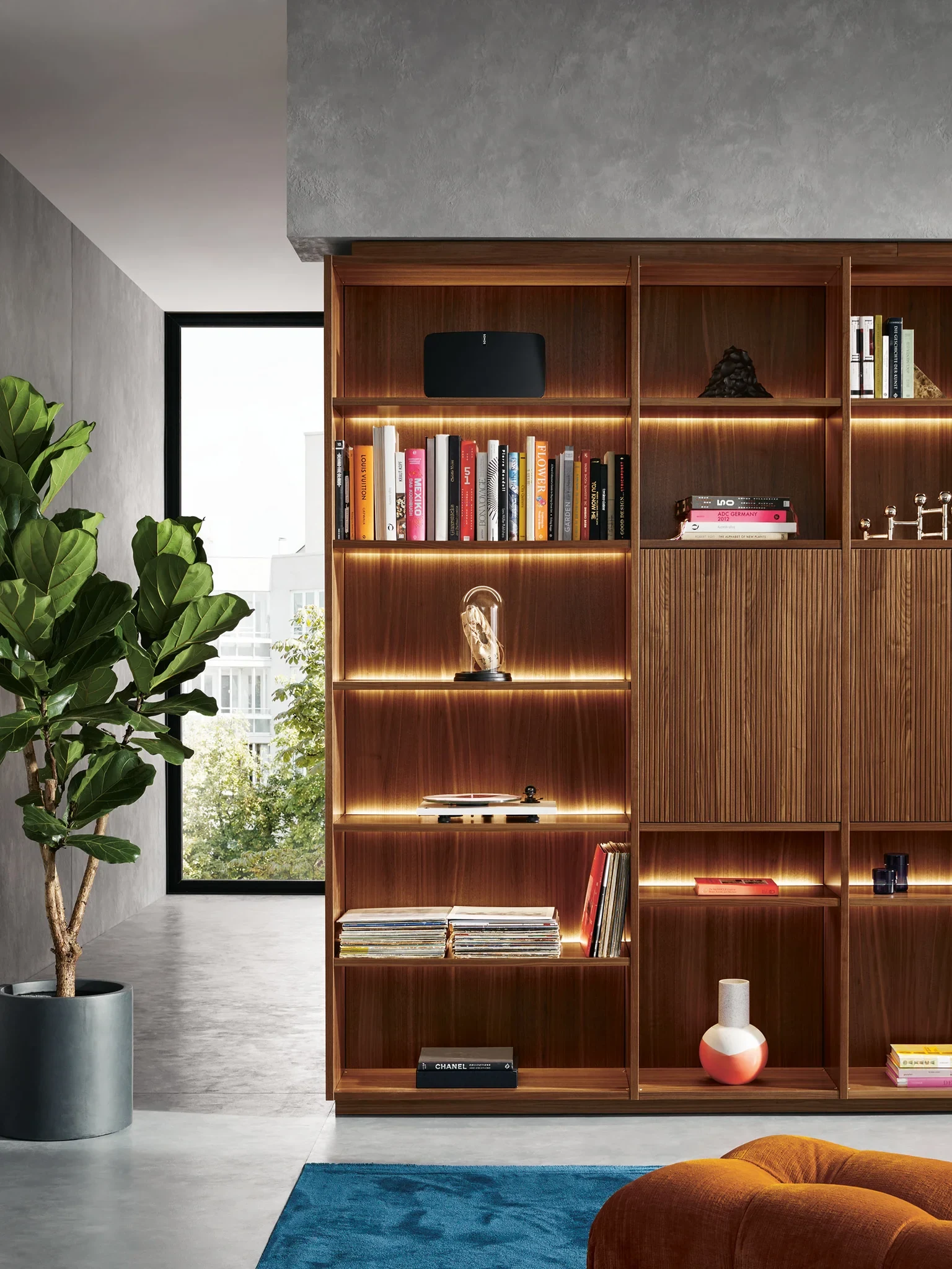 next125: Offenes Holzregal neben einem Fenster mit beleuchteten Regalböden, Büchern und Deko